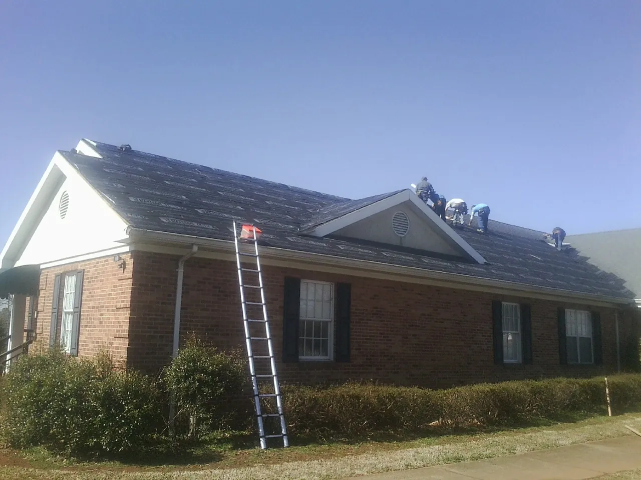 Crew tearing shingles off a brick ranch roof with a ladder set — Metal Roof Repair work by our crew in Westmoreland