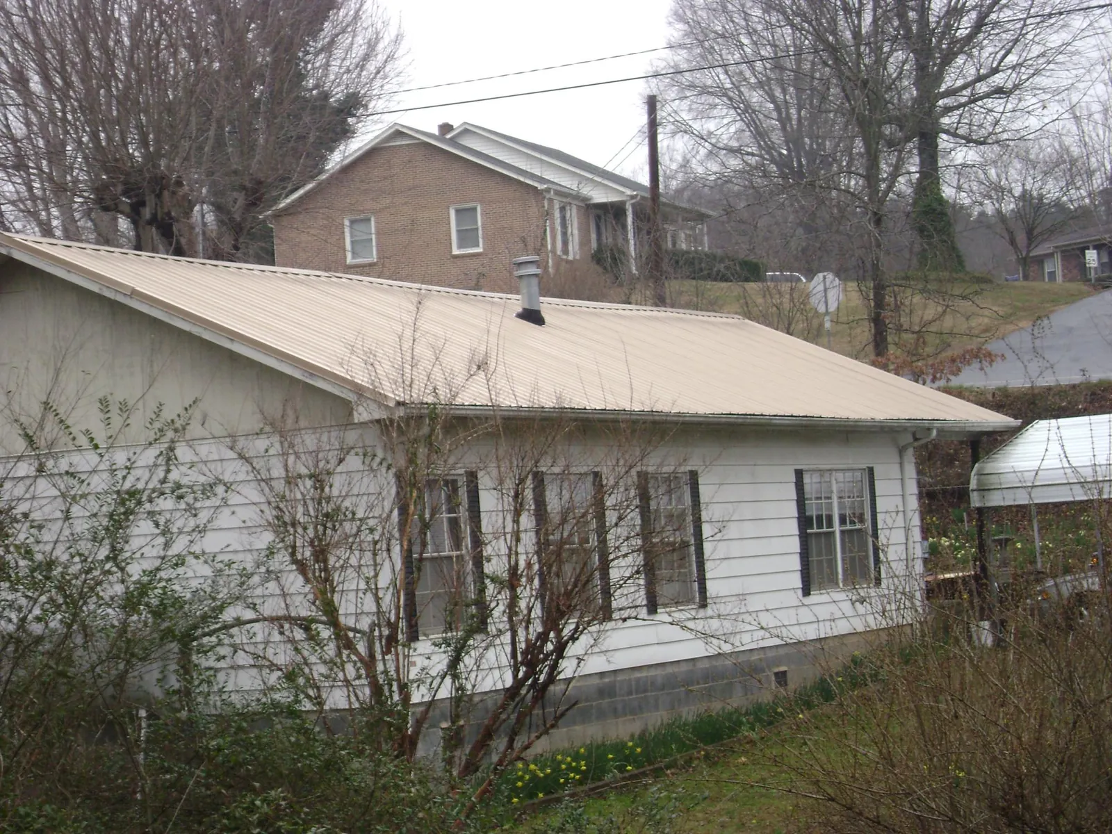 Tan metal roof on a white sided house set into a hillside — Commercial Roofing by Roofing Brothers in Westmoreland